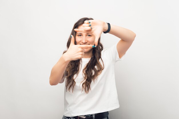 Photo of young woman making photography gesture over white background