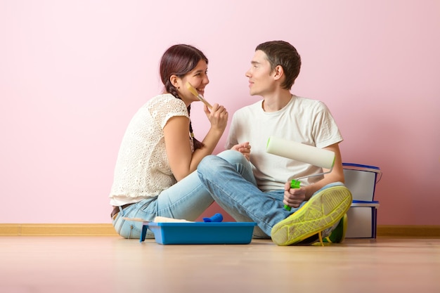 Photo of young woman and man with paint roller sitting on floor