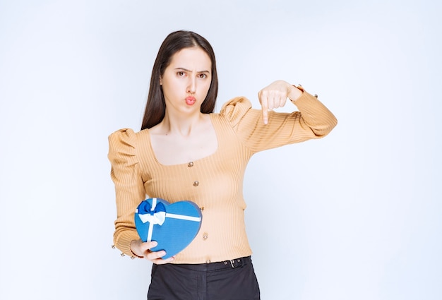 Photo of a young woman model with a heart shaped gift box pointing down.