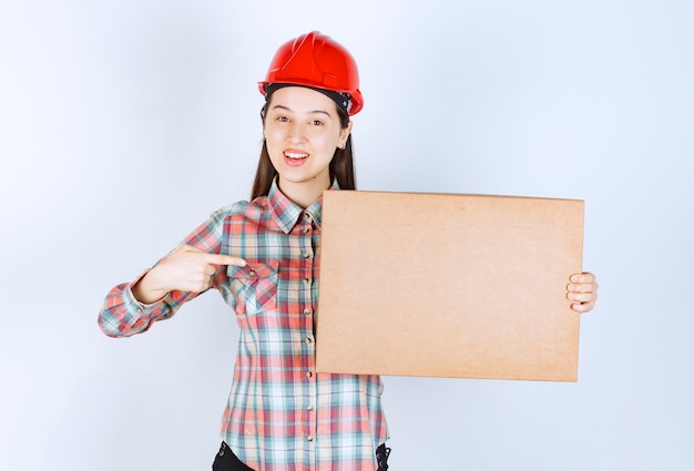 Photo of young woman in red helmet showing carton box. 