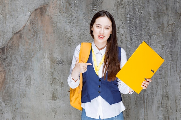 Photo of young woman with yellow backpack holding folder. High quality photo