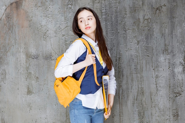 Photo of young woman with yellow backpack standing over wall.\
high quality photo