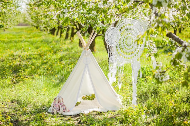 Foto zona fotografica per un servizio fotografico per bambini in un giardino fiorito primaverile wigwam acchiappasogni all'uncinetto e coniglietti