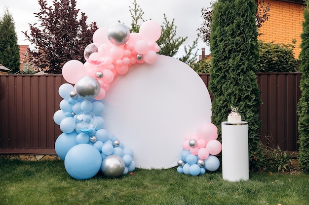 Photo zone for a gender party in the yard of the house Photo zone on the street on a green lawn White circle with pink and blue balls on the background of trees