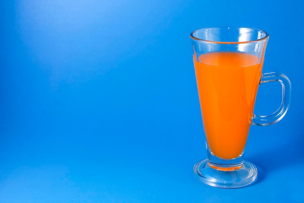 Фотография апельсинового сока в высоком стакане с ручками на синем фоне