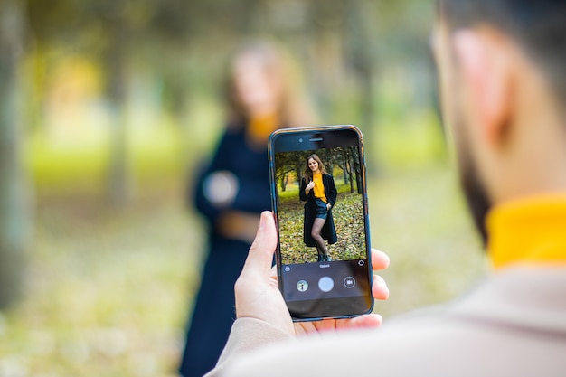 秋の公園で電話でガールフレンドの写真を撮る