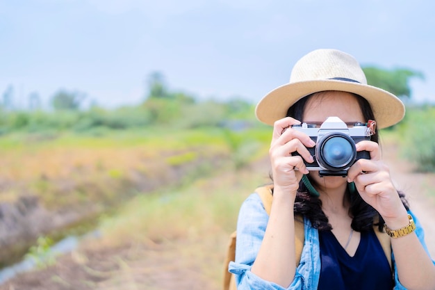 カメラで顔を覆っている写真家アジア人驚くべき黒髪のかわいい陽気な女の子の肖像画屋外カメラを置いて庭で休んでいる女性