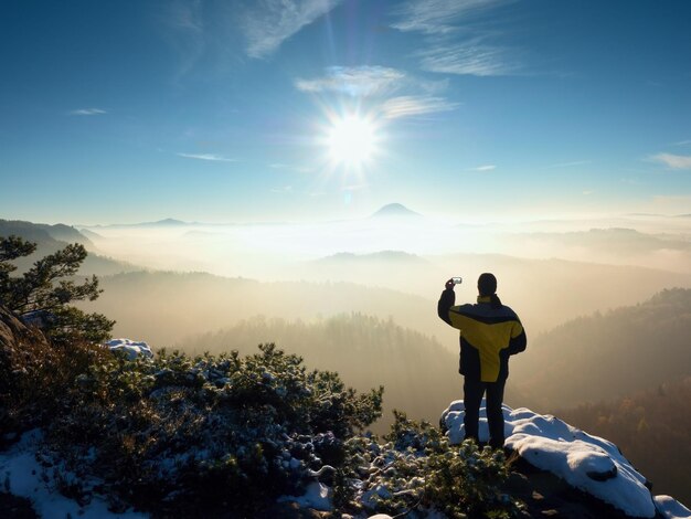 Photo photographer by smart phone takes picture of misty hilly landscape exposed rocks covered with snow