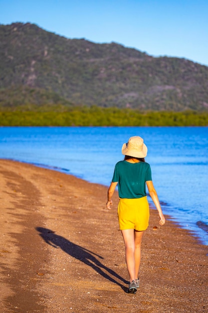 帽子をかぶった写真家の女の子が、オーストラリアの日没時に磁気島の楽園のビーチを歩く