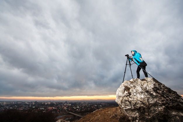 Фотограф стоит со своей камерой на большой скале