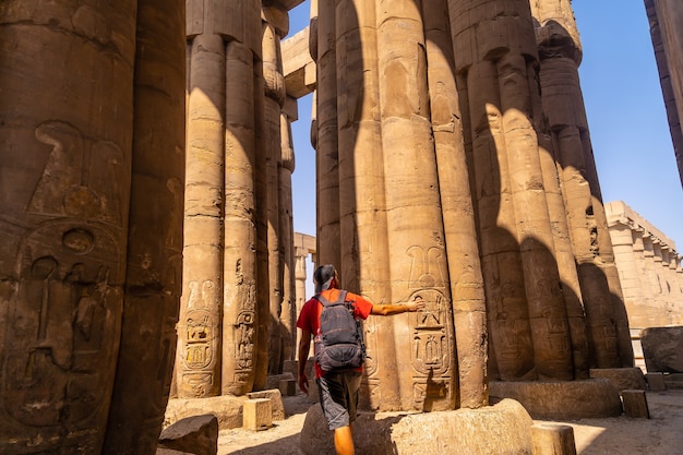 A photographer looking at ancient Egyptian drawings on the columns of the Temple of Luxor, Egypt