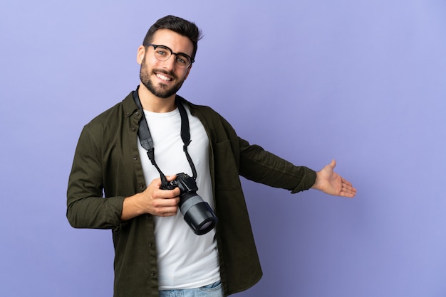 Photographer man over isolated purple wall extending hands to the side for inviting to come