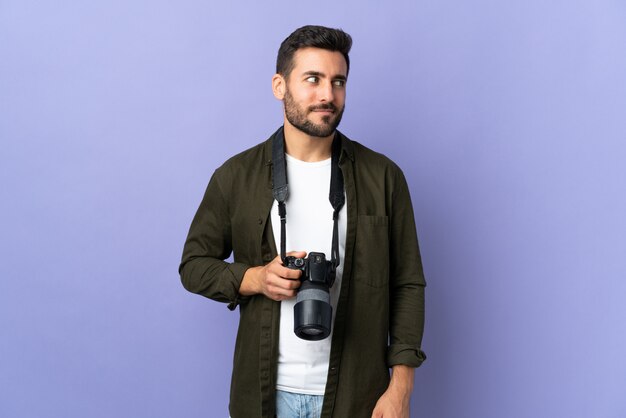 Photographer man over isolated purple wall having doubts while looking side