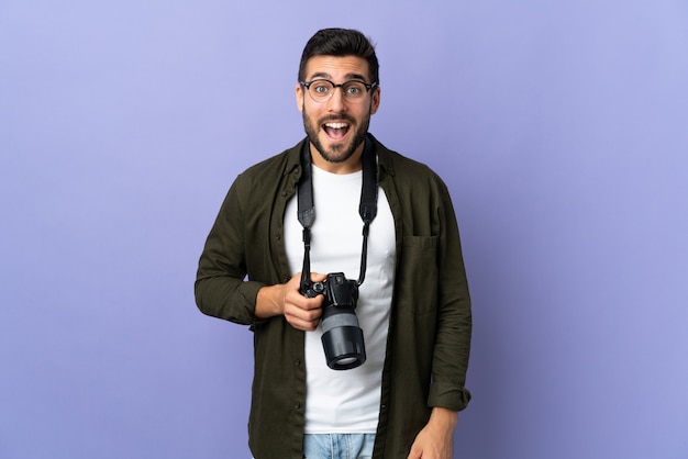 Человек фотографа над изолированной фиолетовой стеной с выражением лица сюрприза