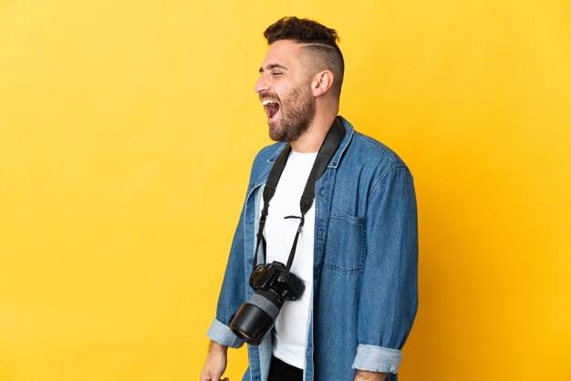 Photographer man isolated on yellow background laughing in lateral position