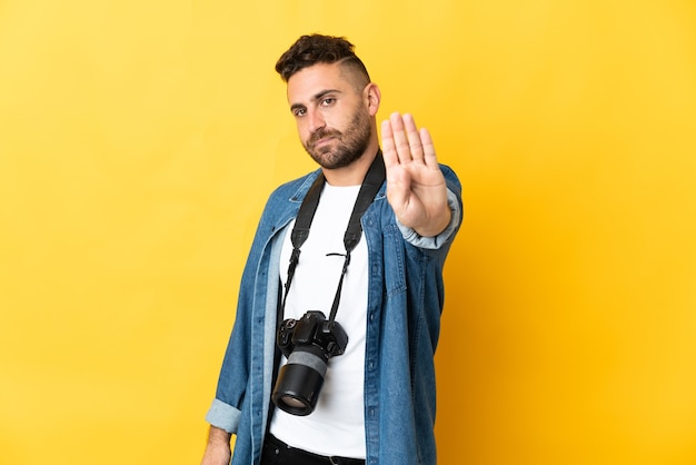 停止ジェスチャーを作る黄色の背景に分離された写真家の男