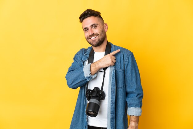 Photographer man isolated on yellow background pointing to the side to present a product