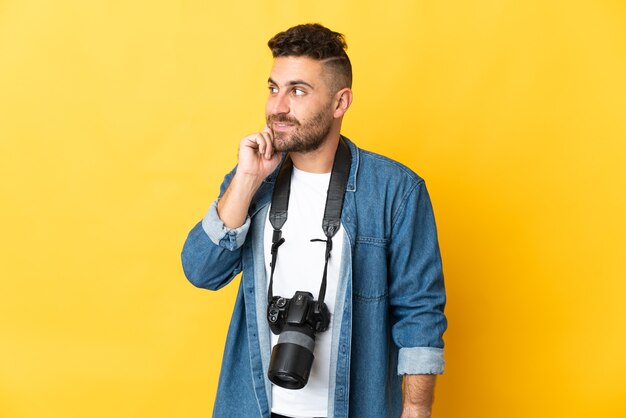 Photographer man isolated on yellow background thinking an idea while looking up