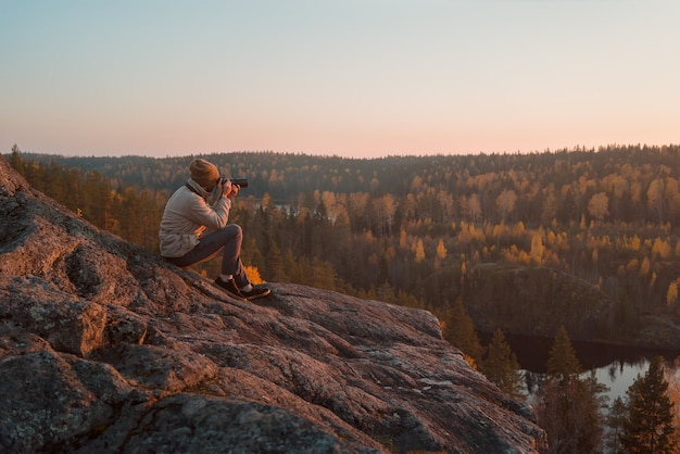 Photographer on the rock takes a photo of the autumn landscape.