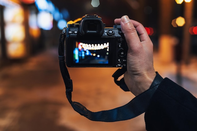 写真家の手は、街の夜に現代のミラーレス カメラで写真を撮る