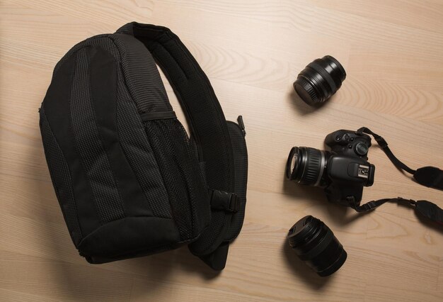 Photo photographer's small backpack with digital slr camera and replaceable lenses on a wooden background