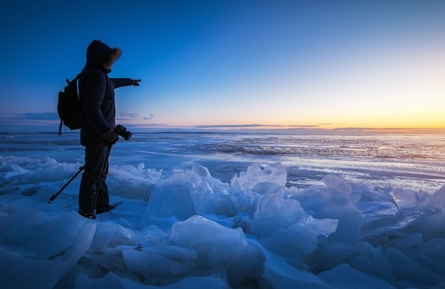 Photo photographer take pictures on the frozen river during sunset. a man points a finger at dawn