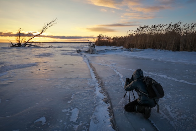 Photographer take pictures on the ice near the shore during sunset