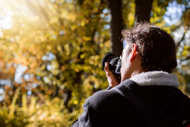 Photo photographer taking pictures in autumn forest against bright sunlight