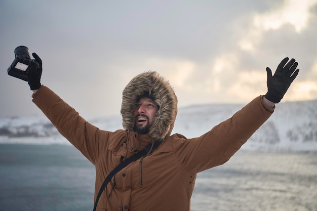 Фото Фотограф-турист-исследователь зимой в ненастную погоду в теплой меховой куртке и фотографирует природу и пейзажи