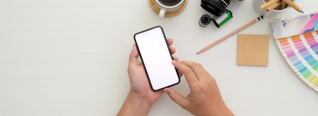 Photographer using mock-up smartphone on white worktable with camera and other supplies