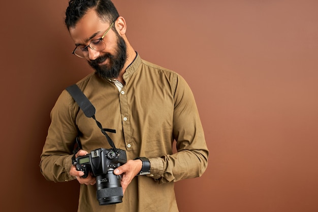 Фотограф с камерой, изолированной на коричневом фоне, успешный профессиональный мужчина смотрит на фотографии на экране камеры. концепция фотографии