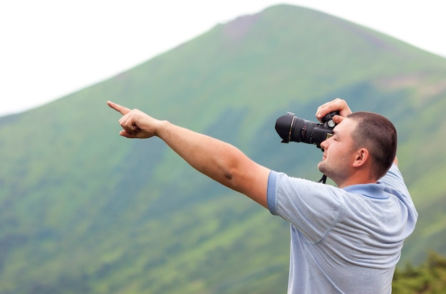 指で指している山の写真を撮るカメラを持つカメラマン