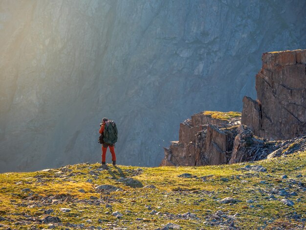 大きなバックパックを持った写真家が崖の端にある美しい山の風景を撮影します。日没の危険な山々と深淵。