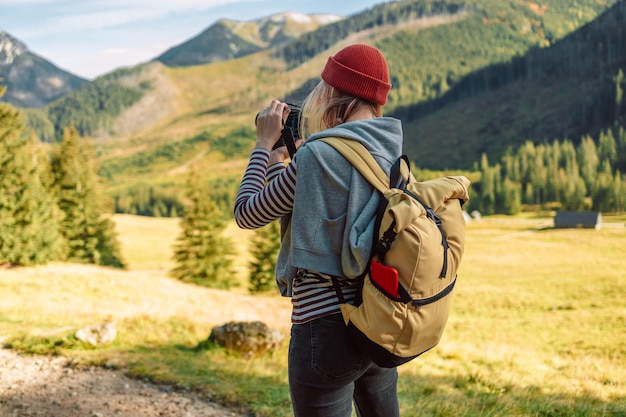 黄色のバックパックを持つ写真家の女性がタトラ山脈の秋の風景の写真を撮っています