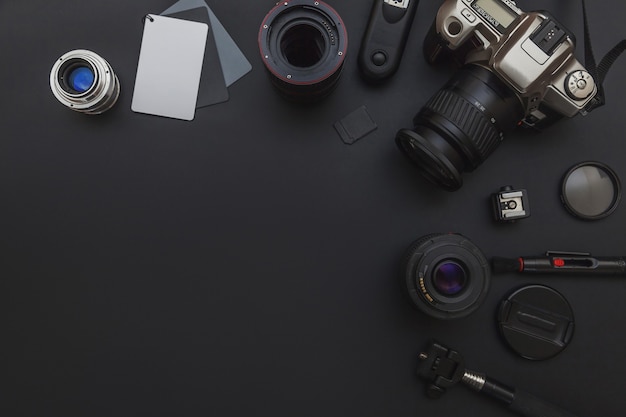 Posto di lavoro del fotografo con sistema di fotocamera dslr, kit di pulizia della fotocamera, obiettivo e accessorio della fotocamera su sfondo nero scuro