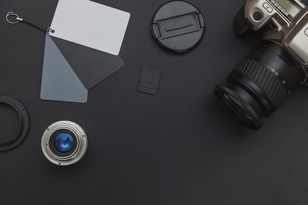 Photographer workplace with dslr camera system, camera cleaning kit, lens and camera accessory on dark black table background. Hobby travel photography concept. Flat lay top view copy space