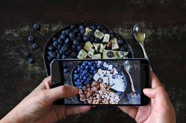 Photographing a healthy meal on a mobile phone. Cheese plate with blueberries and nuts.