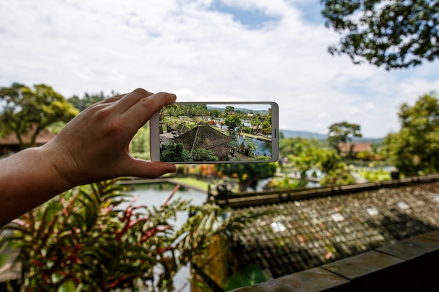 スマートフォンを手にした写真。旅行のコンセプト。バリ島のティルタガンガの水の宮殿。