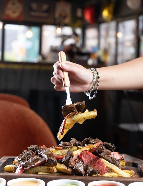 Photographs of hands eating a mixed salchipapa at the table of a steakhouse