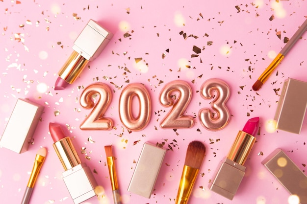 Photography from above of rose gold numbers 2023 with makeup accessories around