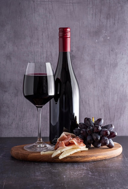 古い灰色の背景のボトルブドウチーズ生ハムのガラスの赤ワインの写真