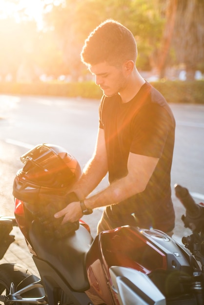 Photography sun reflect of young rider putting on gloves to ride his motorbike on the city.