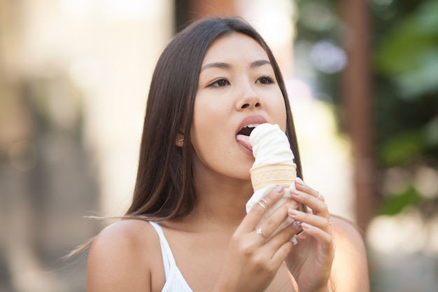 アイスクリームを食べて暑い中に立つアジアの女性の写真。感情的な幸せ。顔に焦点を当てます。