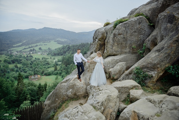 Photoshoot of a couple in love in the mountains. The girl is dressed like a bride in a wedding dress.