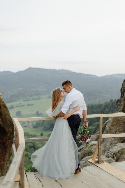 Photoshoot of a couple in love in the mountains. The girl is dressed like a bride in a wedding dress.