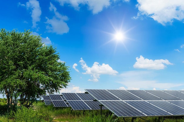 ツリーグリーンの太陽光発電モジュール太陽光発電所は、白い雲の背景、代替エネルギーの概念、クリーンエネルギーを備えた風景の景色の春に牧草地を残します。