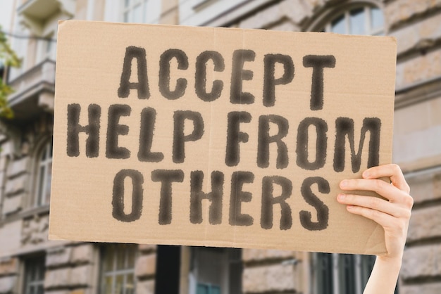 The phrase Accept help from others on a banner in men's hand with blurred background Admit Share Deal Rescue Agree Deed Focus Trust Team Reach Need Effort Action Hand Help Raise