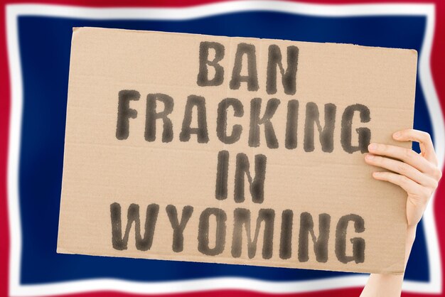 Photo the phrase ban fracking in wyoming on a banner in men's hand with blurred wyoming flag on the background nature extract stop pipe energy drill raw power fuel fossil crisis