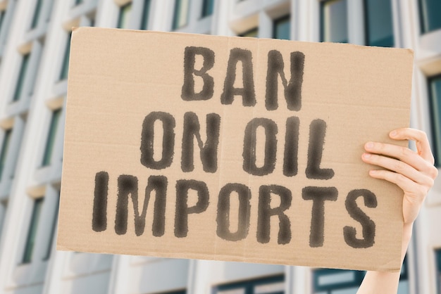 The phrase Ban on oil imports on a banner in men's hand with blurred background Rise Law Flow Money North War Value Pipeline Gas Crash Cargo Iran Price Block Stop Pipe Crisis