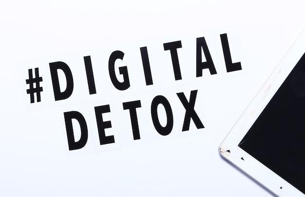 Phrase Digital detox and craced tablet. White background,hashtag, top view.